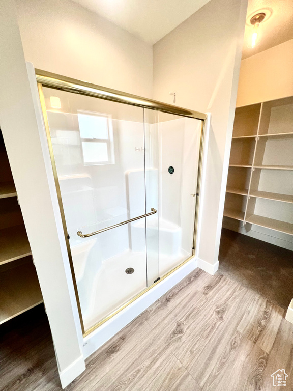 Full bathroom featuring baseboards, wood finished floors, a spacious closet, and a shower stall