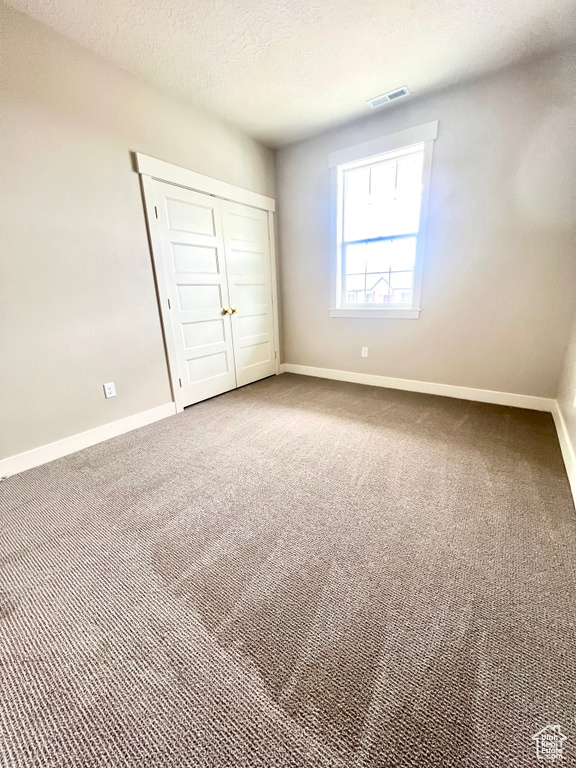 Unfurnished bedroom with a textured ceiling, visible vents, baseboards, a closet, and carpet