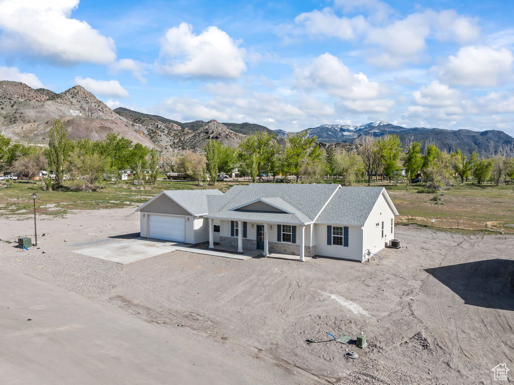 View of front facade featuring roof with shingles, a garage, dirt driveway, a porch, and a mountain view