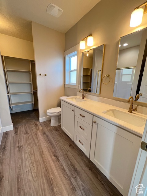Bathroom featuring wood finished floors, double vanity, baseboards, and toilet