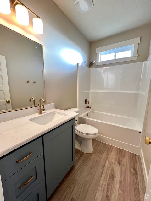 Bathroom featuring wood finished floors, vanity, toilet, and  shower combination