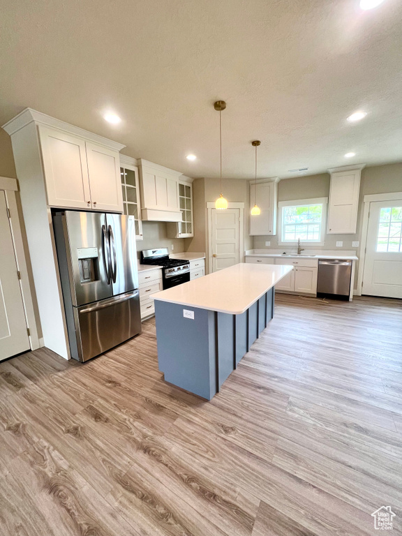 Kitchen with appliances with stainless steel finishes, a sink, light wood-style floors, light countertops, and white cabinetry