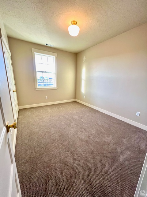 Spare room with carpet floors, a textured ceiling, and baseboards