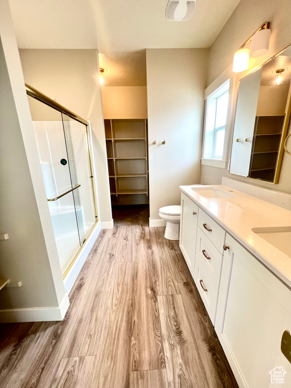 Full bathroom with double vanity, a walk in closet, a shower stall, wood finished floors, and baseboards