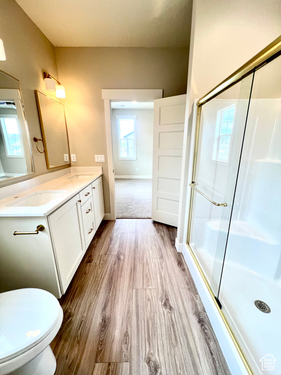Bathroom featuring double vanity, wood finished floors, baseboards, a sink, and a stall shower