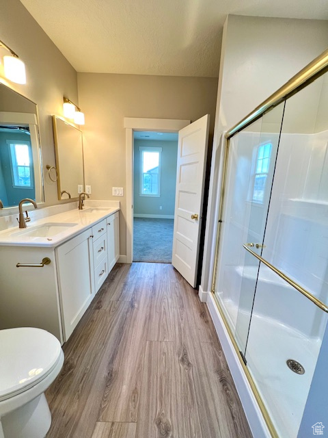 Bathroom featuring wood finished floors, toilet, double vanity, a stall shower, and a textured ceiling