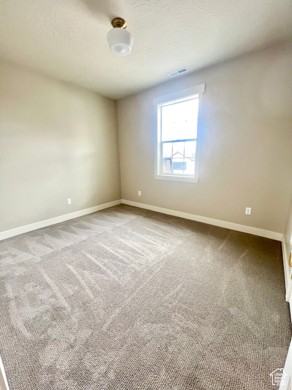 Spare room with baseboards, a textured ceiling, carpet, and visible vents