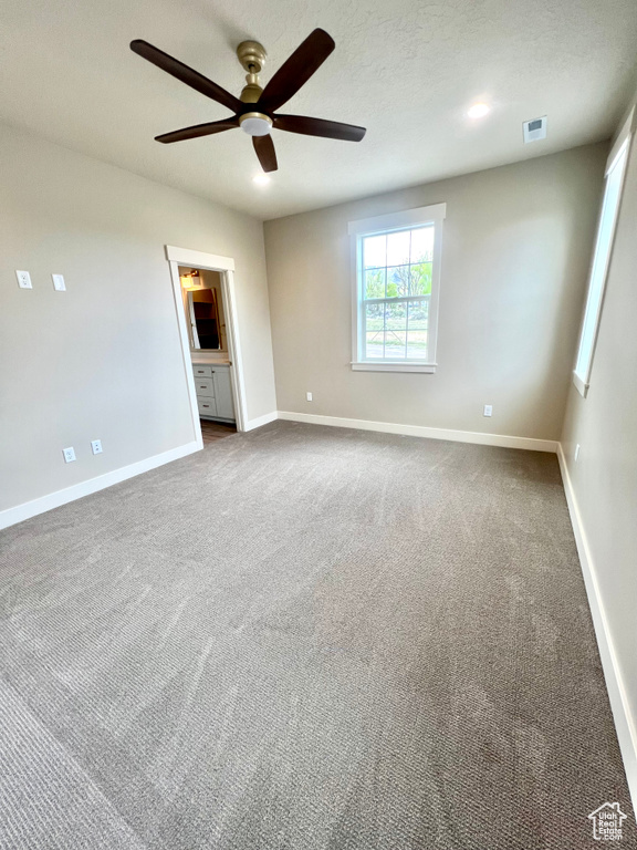 Empty room with visible vents, a ceiling fan, baseboards, and dark carpet