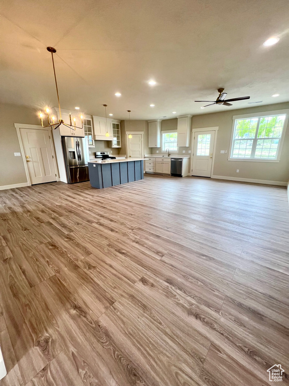 Unfurnished living room featuring recessed lighting, baseboards, wood finished floors, and ceiling fan with notable chandelier