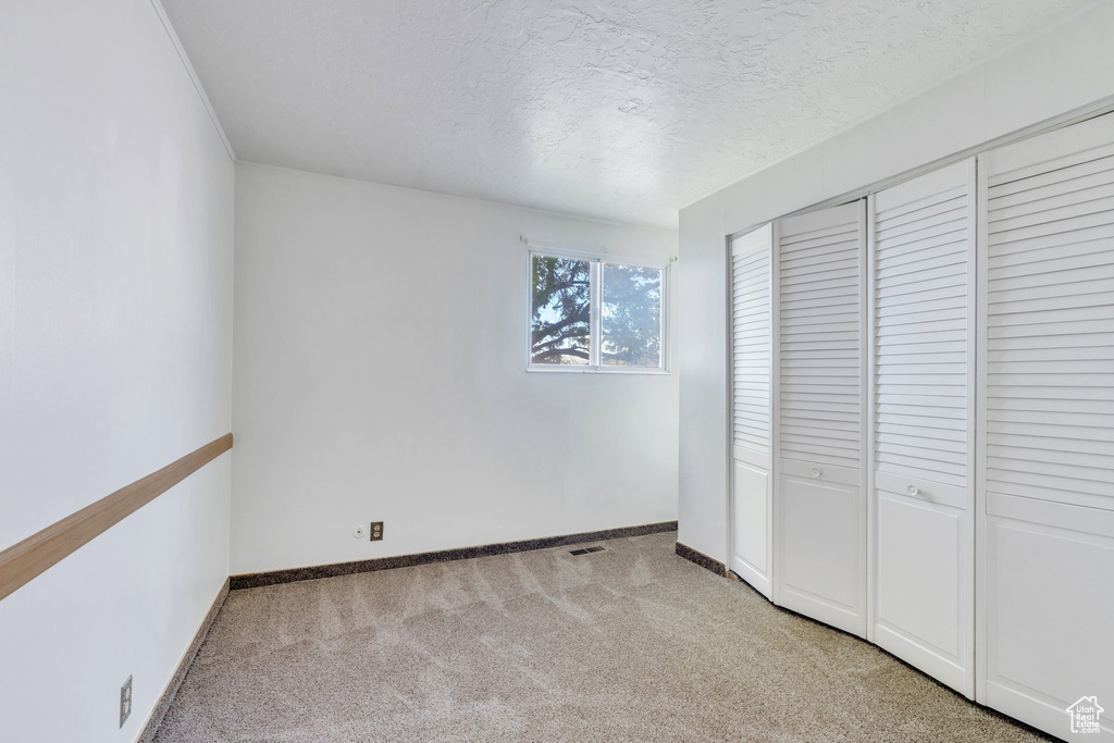 Unfurnished bedroom featuring baseboards, light carpet, a closet, and a textured ceiling