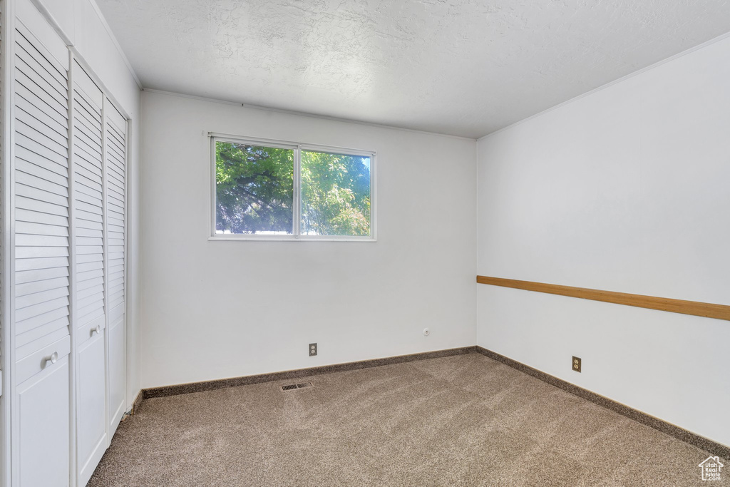 Unfurnished bedroom featuring a textured ceiling, carpet, baseboards, visible vents, and a closet