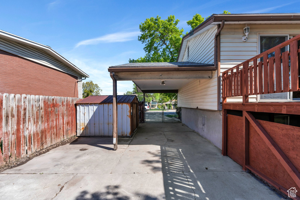 View of patio / terrace with a storage shed, a carport, fence, an outdoor structure, and concrete driveway