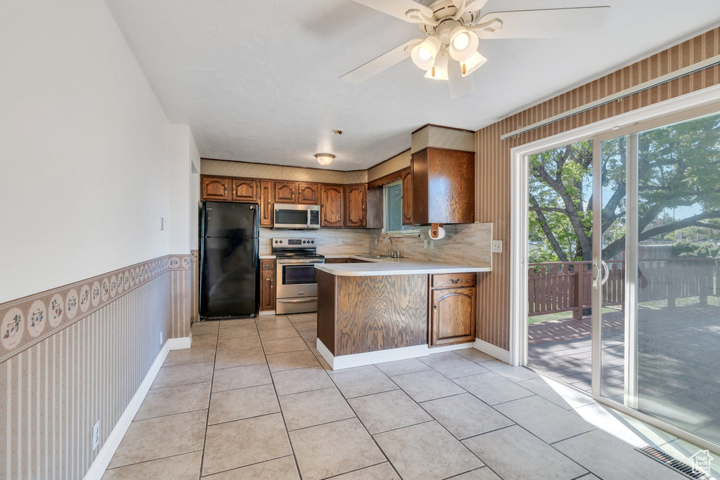Kitchen with brown cabinetry, a peninsula, light countertops, a sink, and stainless steel appliances