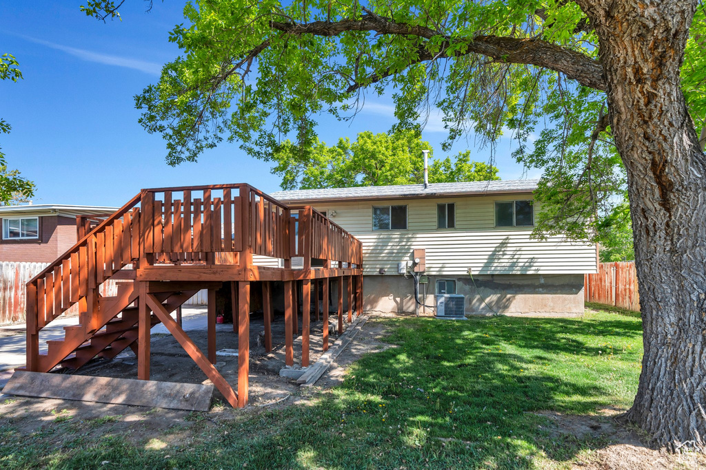 Rear view of house featuring a wooden deck, fence, stairs, a lawn, and central air condition unit