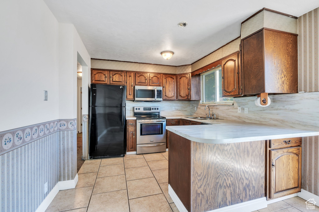 Kitchen with brown cabinets, appliances with stainless steel finishes, a sink, light countertops, and a peninsula
