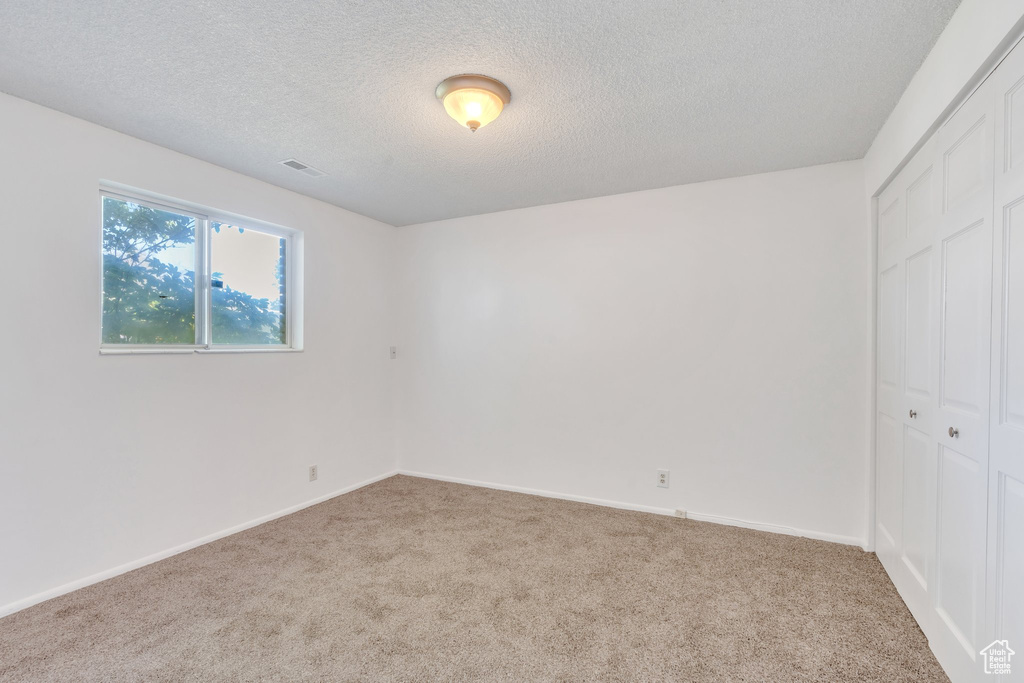 Unfurnished bedroom with a textured ceiling, visible vents, carpet, and a closet