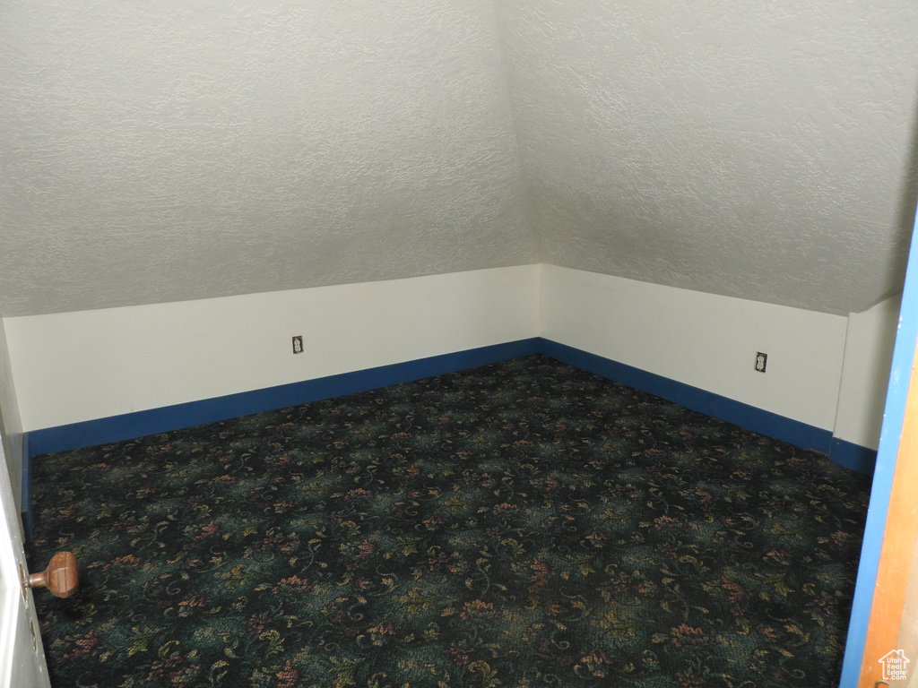 Carpeted empty room with baseboards, a textured ceiling, and lofted ceiling