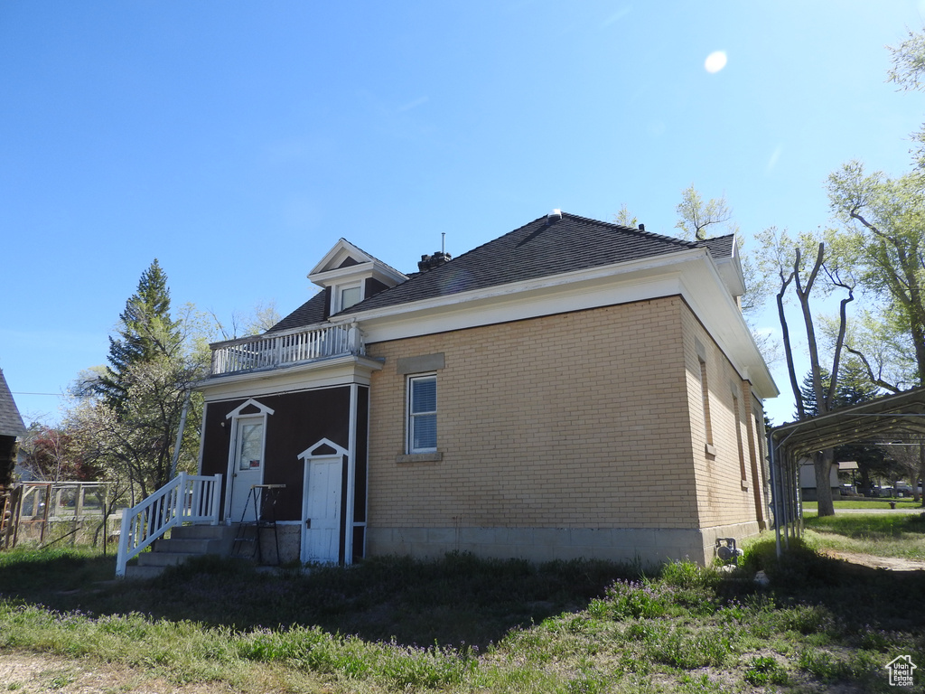 Rear view of house featuring brick siding, a balcony, and roof with shingles