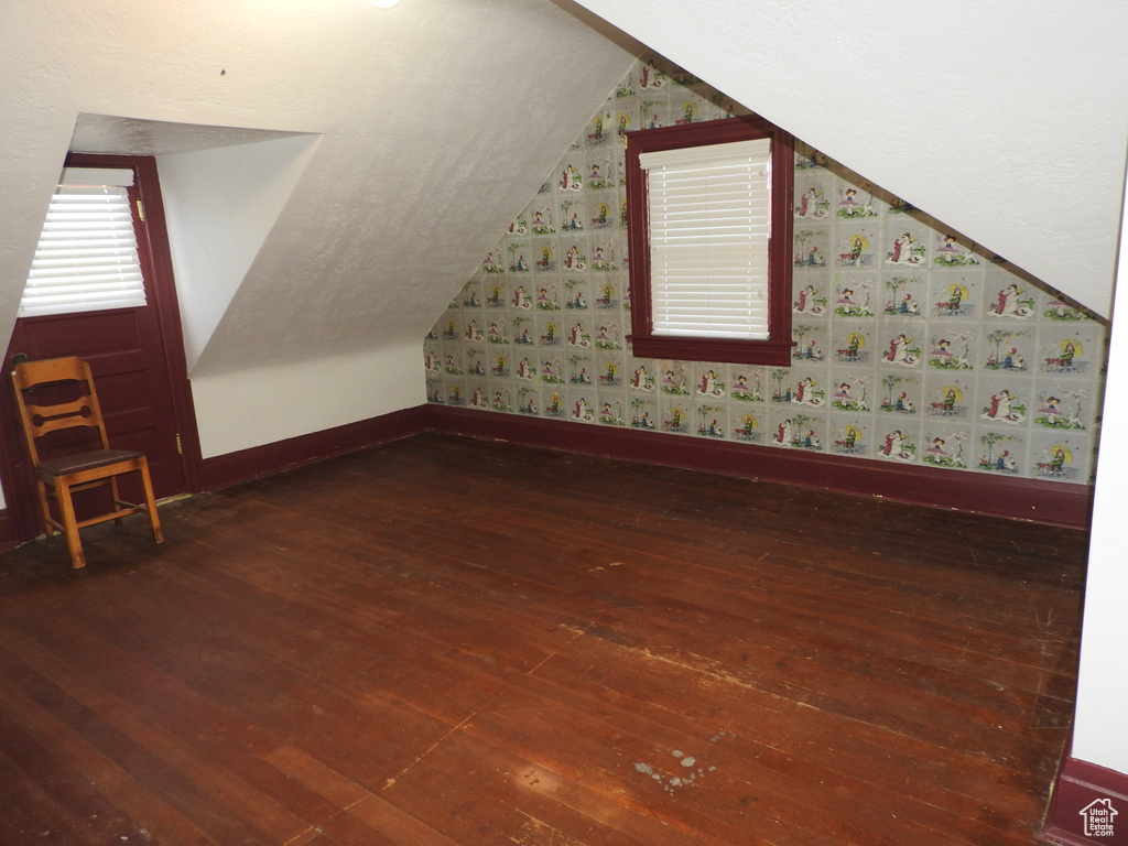 Bonus room featuring baseboards, vaulted ceiling, wallpapered walls, and hardwood / wood-style floors