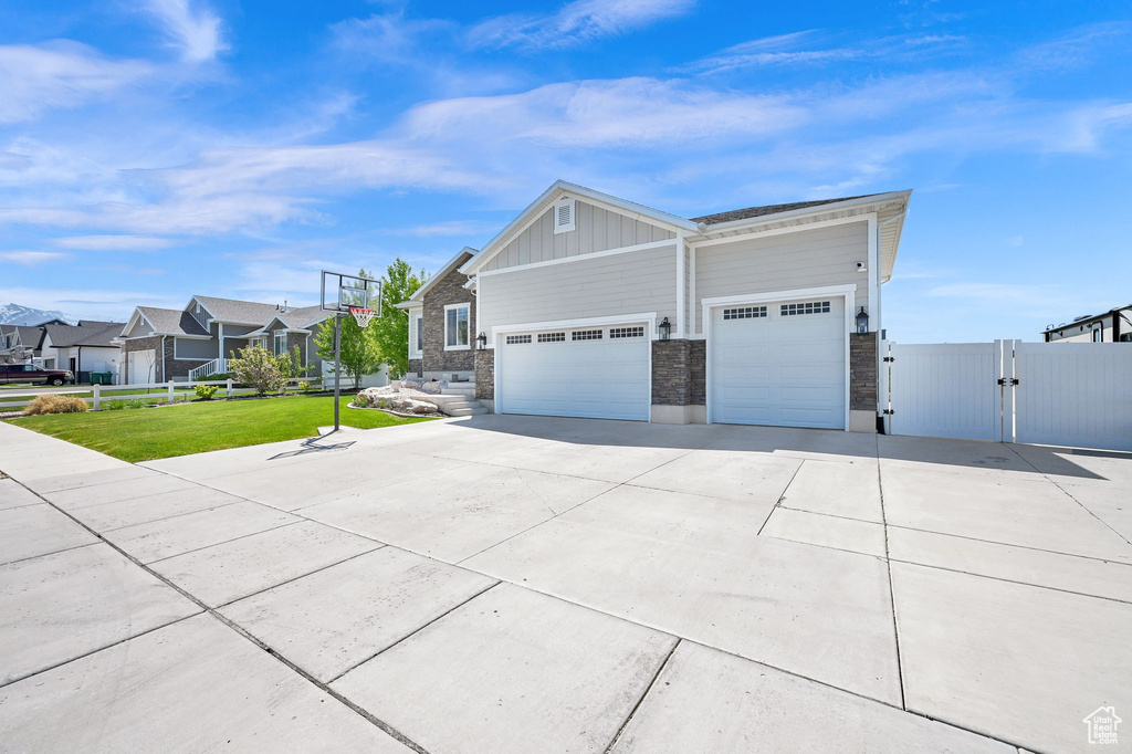 View of side of home featuring board and batten siding, driveway, a gate, fence, and a yard