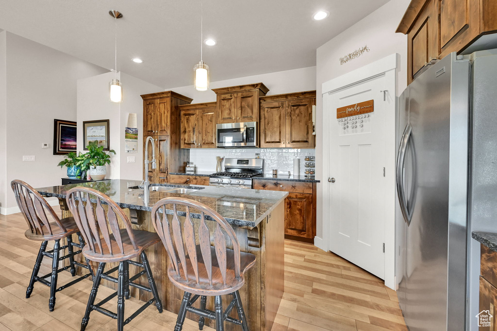 Kitchen with brown cabinets, appliances with stainless steel finishes, a sink, decorative backsplash, and light wood-type flooring