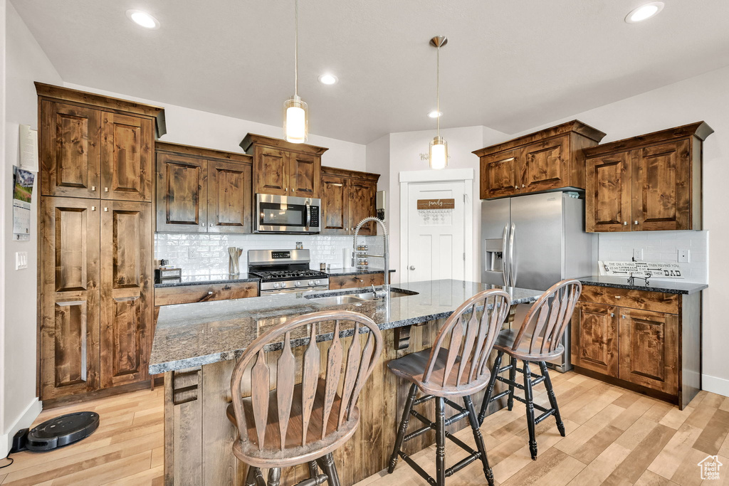 Kitchen with a sink, appliances with stainless steel finishes, decorative backsplash, and light wood-style floors