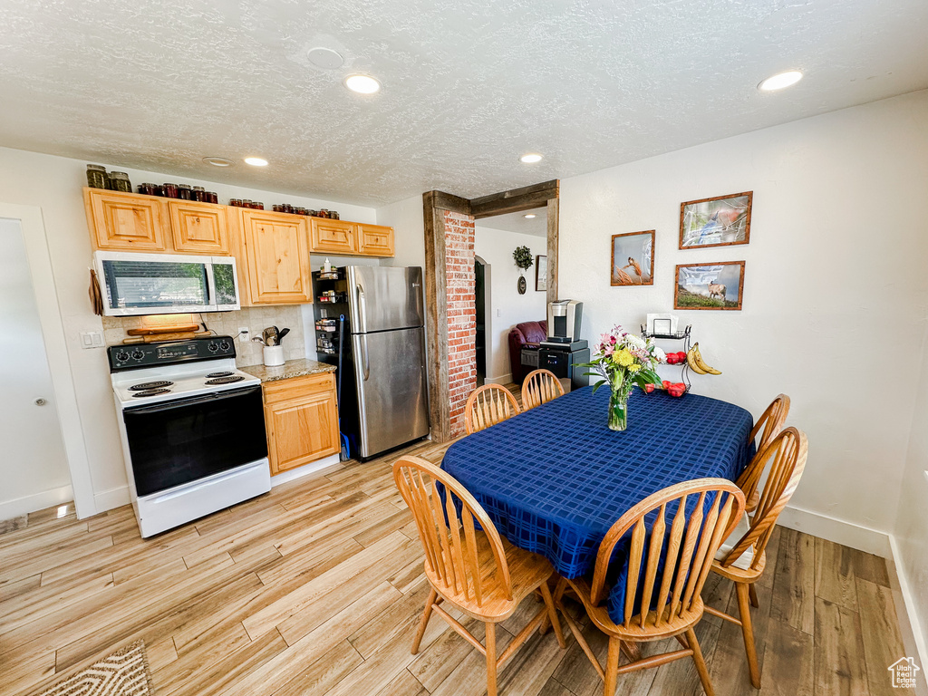 Kitchen with a textured ceiling, appliances with stainless steel finishes, tasteful backsplash, baseboards, and light wood finished floors