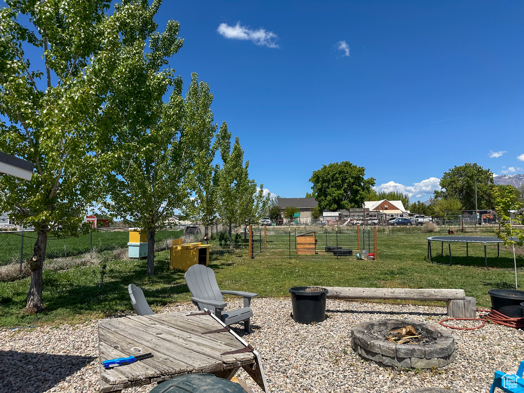 View of yard with fence, a trampoline, and a fire pit