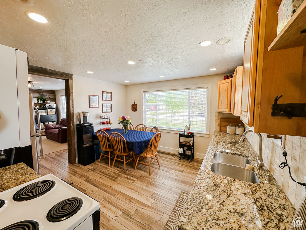 Kitchen featuring light brown cabinets, white electric range, a textured ceiling, a sink, and light wood finished floors
