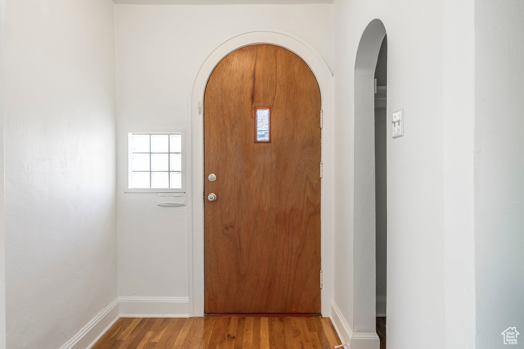 Foyer entrance with arched walkways, baseboards, a healthy amount of sunlight, and wood finished floors