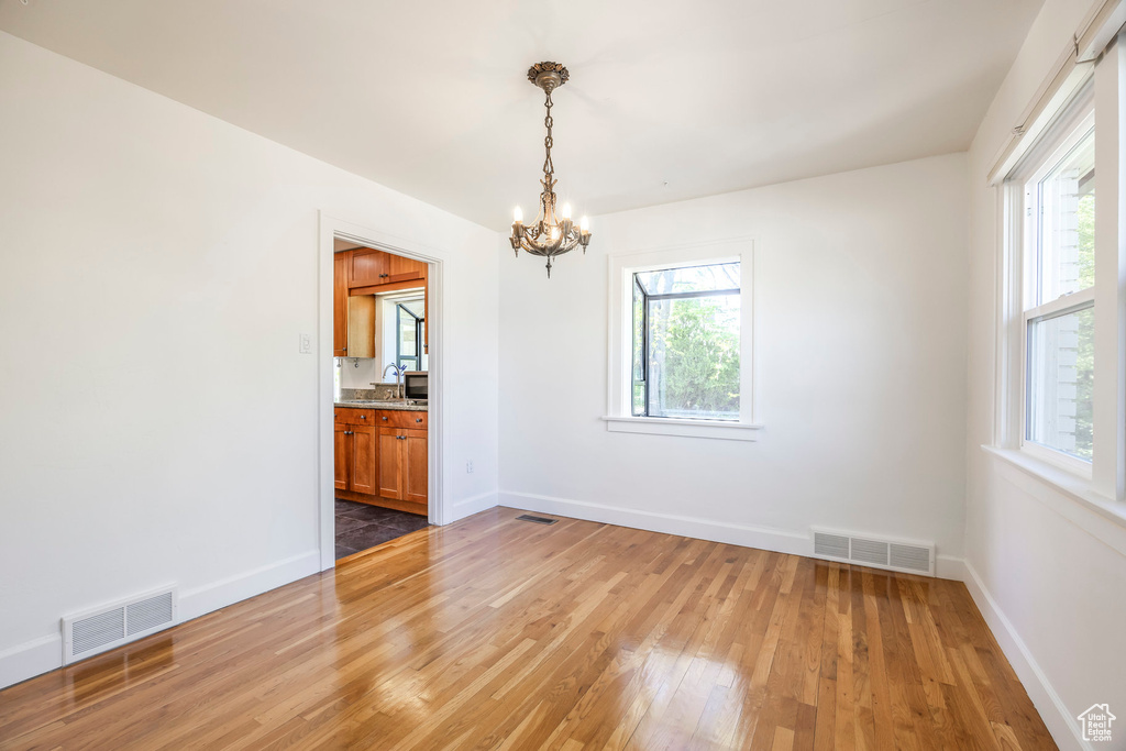 Empty room with a chandelier, visible vents, a wealth of natural light, and light wood-style flooring