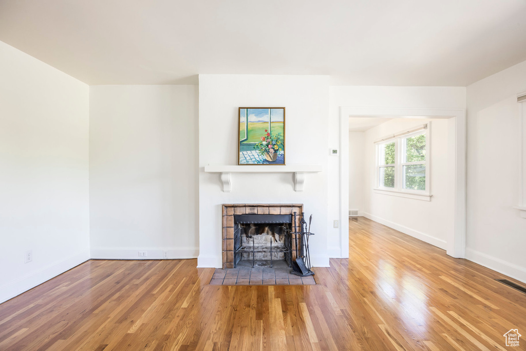 Unfurnished living room with baseboards, visible vents, a tiled fireplace, and wood finished floors
