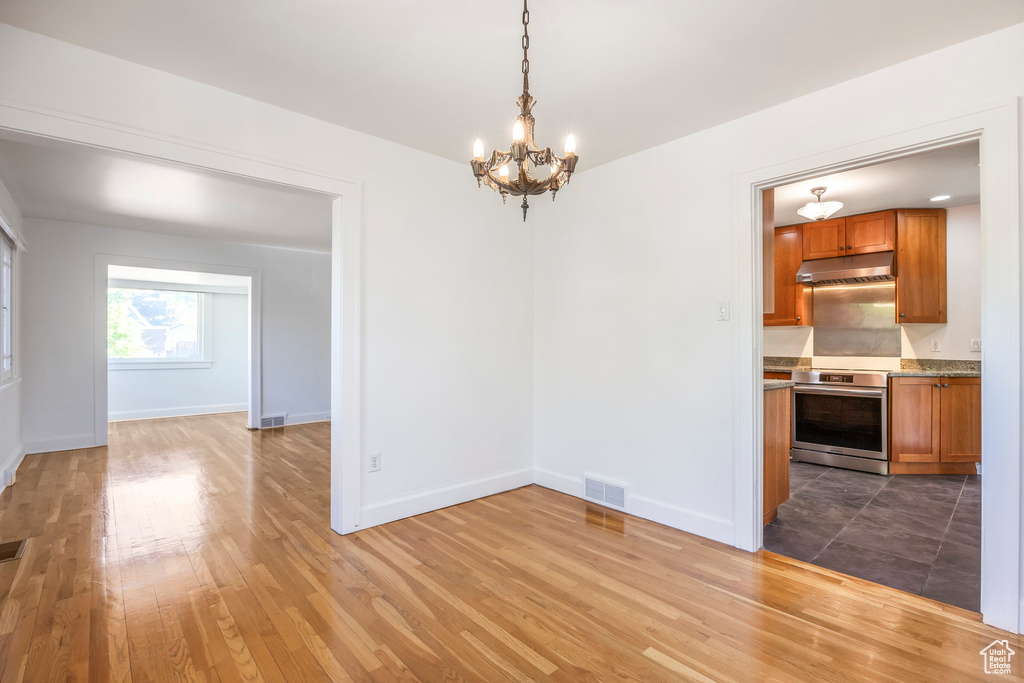Unfurnished dining area with visible vents, light wood finished floors, baseboards, and a notable chandelier