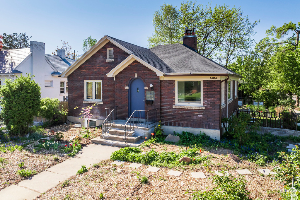 Bungalow-style home with fence, a chimney, a shingled roof, and brick siding