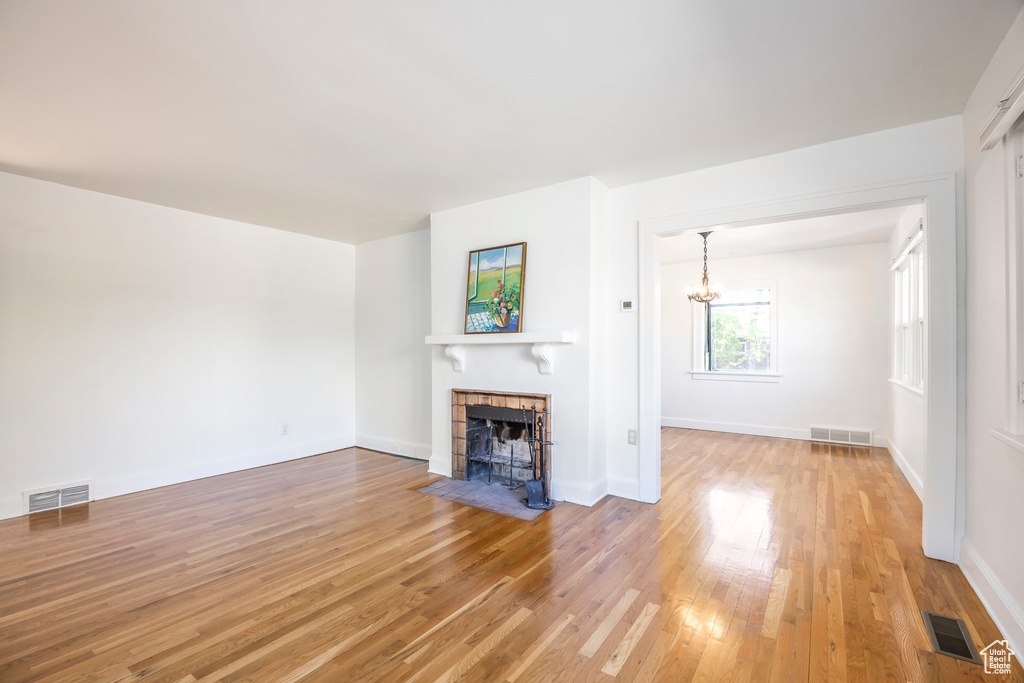 Unfurnished living room with a tiled fireplace, light wood-type flooring, and visible vents