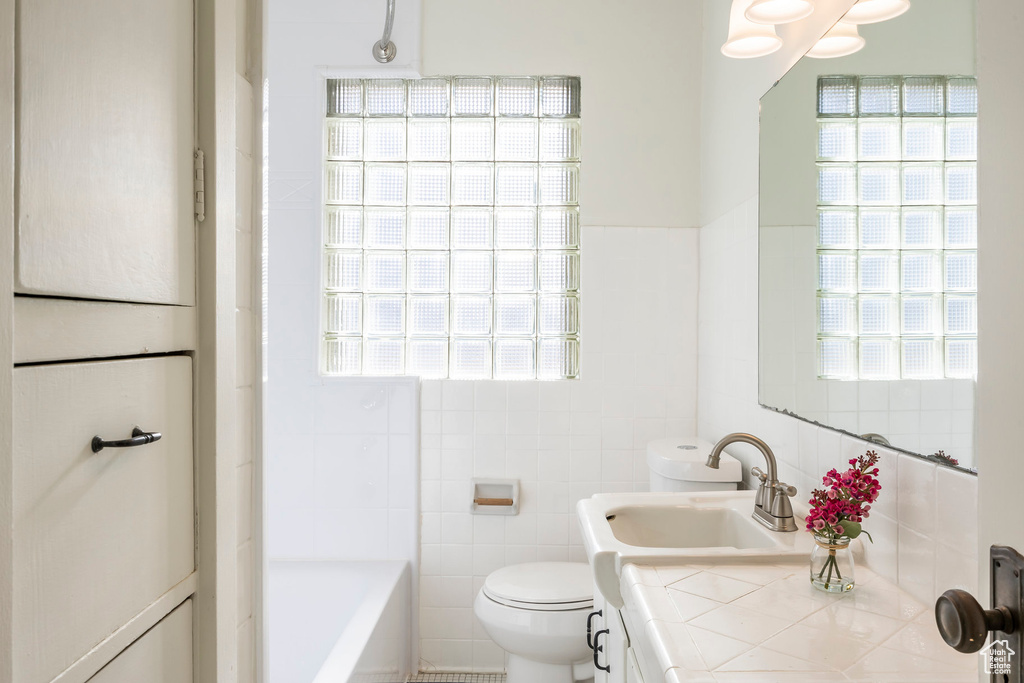 Bathroom featuring toilet, tile walls, plenty of natural light, and vanity