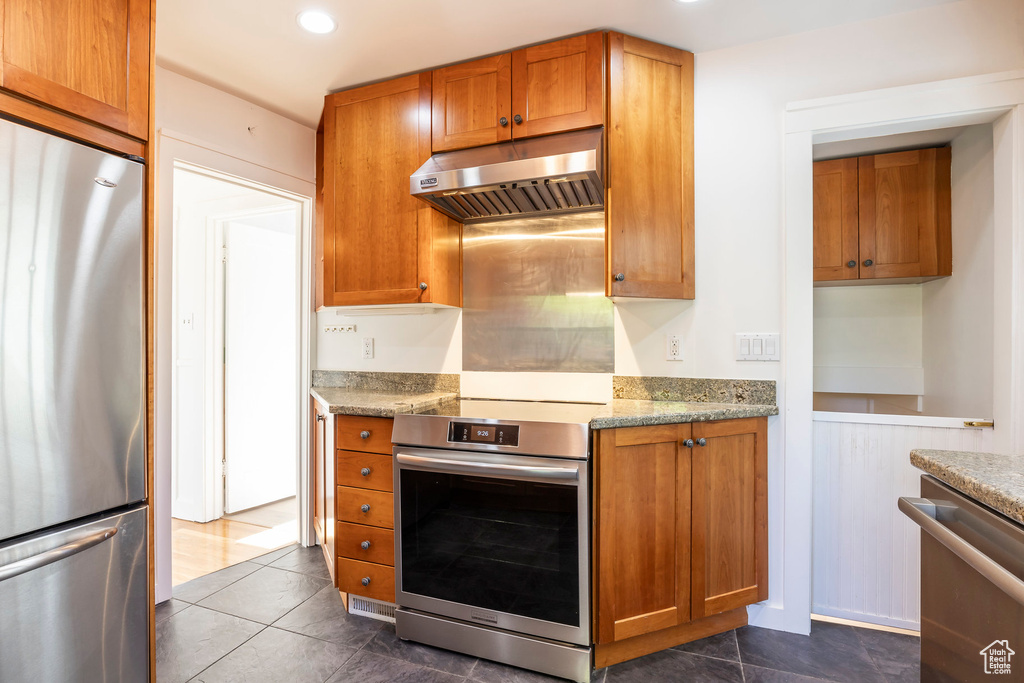 Kitchen with under cabinet range hood, brown cabinets, and appliances with stainless steel finishes