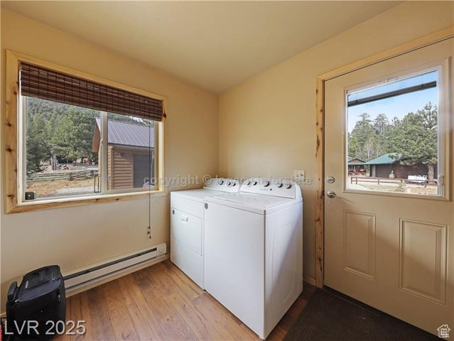 Washroom featuring washing machine and clothes dryer, laundry area, a baseboard heating unit, and light wood-type flooring