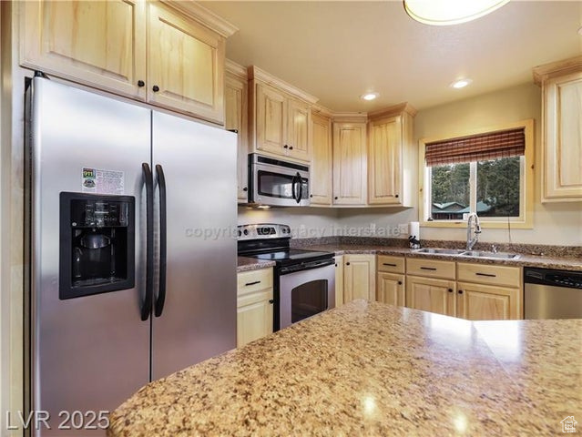 Kitchen featuring light stone counters, appliances with stainless steel finishes, a sink, light brown cabinets, and recessed lighting