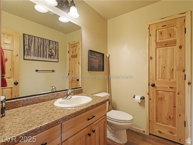 Half bathroom with vanity, wood finished floors, and toilet