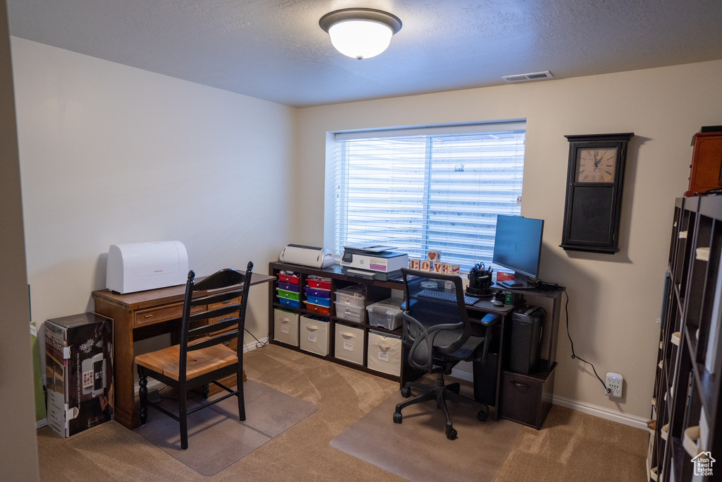 Carpeted home office featuring visible vents, a textured ceiling, and baseboards