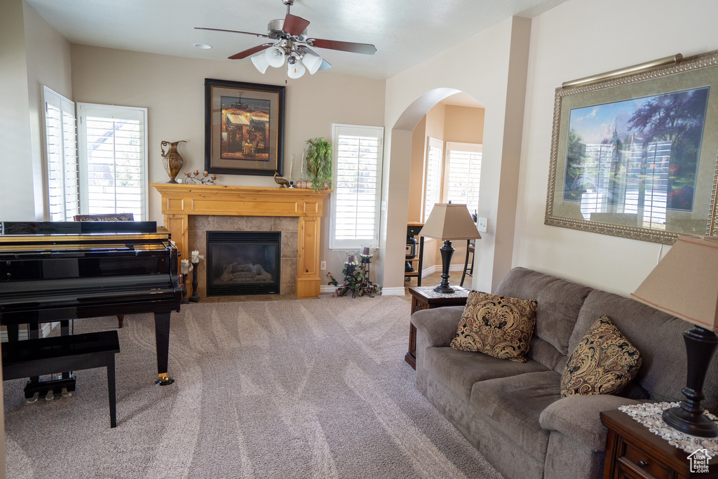 Carpeted living room featuring arched walkways, a ceiling fan, and a tile fireplace