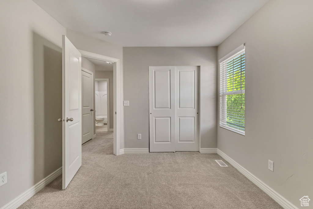 Unfurnished bedroom with baseboards, visible vents, and light colored carpet