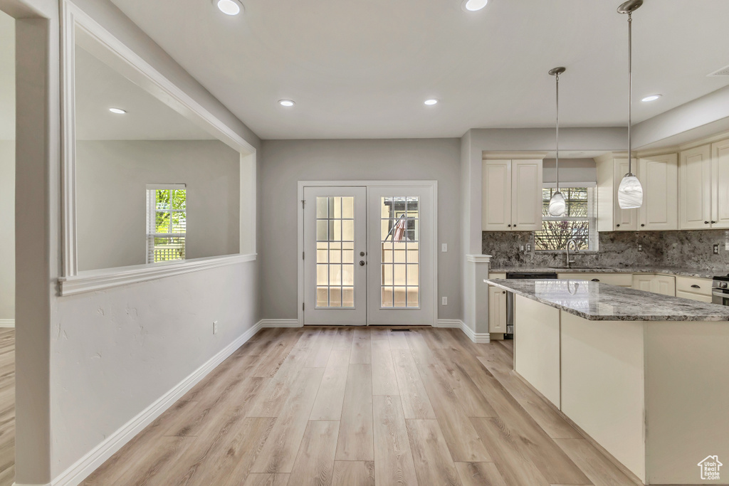 Kitchen with light stone countertops, decorative backsplash, light wood-type flooring, decorative light fixtures, and french doors