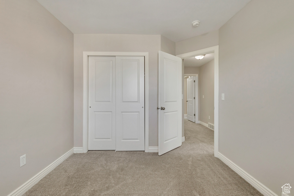 Unfurnished bedroom with baseboards, visible vents, a closet, and light colored carpet