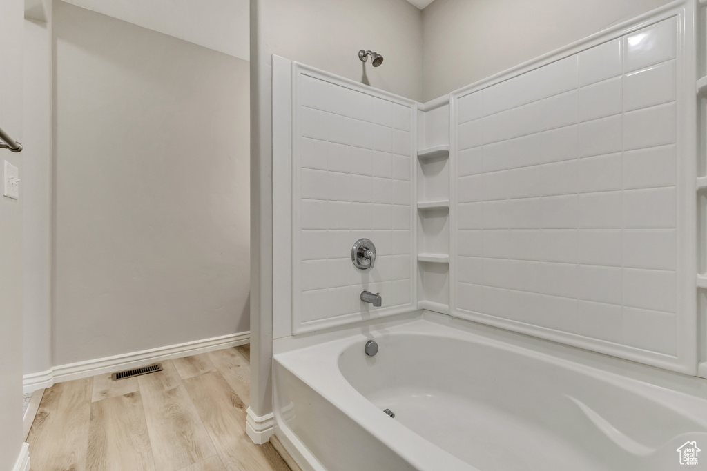 Full bathroom with wood finished floors, shower / bathtub combination, visible vents, and baseboards