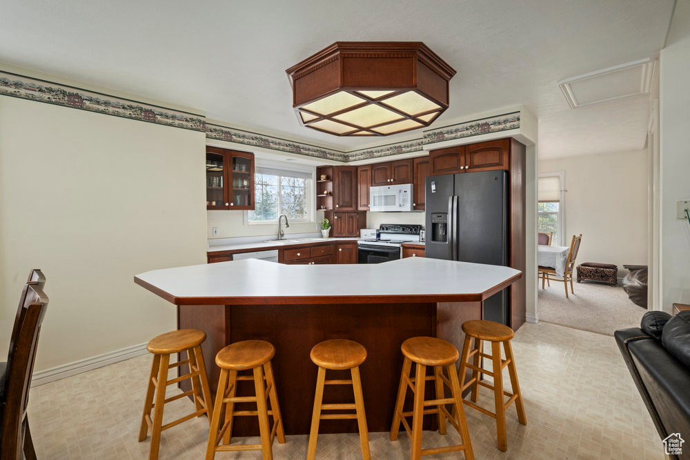 Kitchen with electric range oven, light countertops, a breakfast bar area, white microwave, and glass insert cabinets