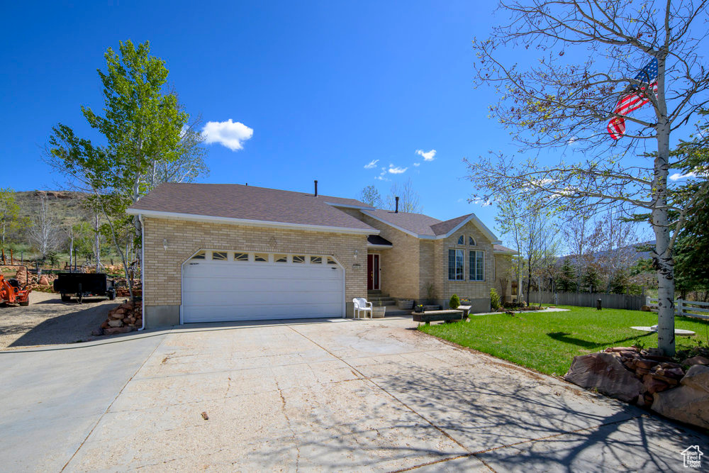 Single story home featuring a garage, a front lawn, fence, brick siding, and driveway
