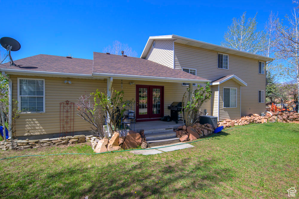 View of front facade with central AC unit, a front lawn, roof with shingles, and french doors