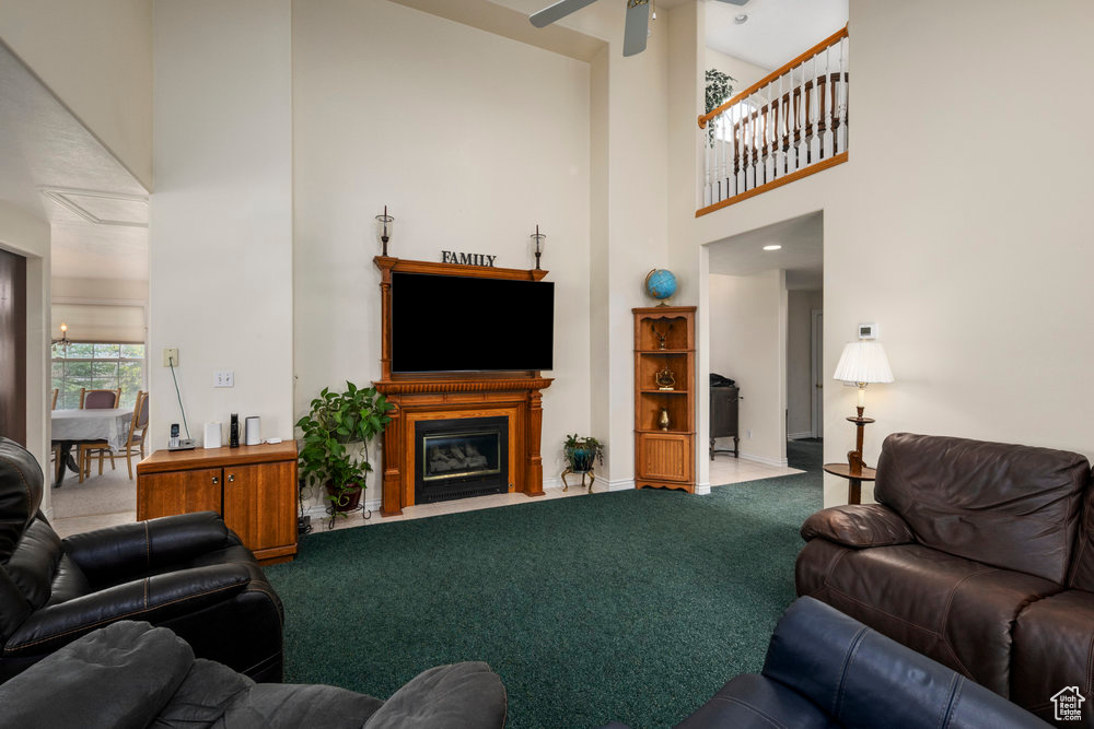 Carpeted living area featuring baseboards, a high ceiling, a fireplace with flush hearth, and ceiling fan